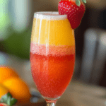Sunrise Strawberry Mimosa with vibrant red and orange layers, served in a champagne flute and garnished with a fresh strawberry.